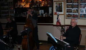 Dave Barnes (piano) looking pensive ('Hey Robin, can I choose what we are playing next please?'). Seen here with Roger Curphey (d.bass) and Alan Clarke (drums). Phoenix Dixieland Jazz Band at Farnborough Jazz Club (Kent) 22jan2015. Photo by Mike Witt.