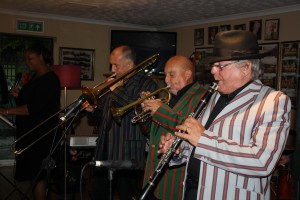 Marlene Hill (vocs) with Paul Taylor (trmb), Mike ‘Megs’ Etherington (trmpt&vocs) and Tony Carter (reeds&vocs), front line of Harry Strutters Hot Seven at Farnborough Jazz Club 7th August 2015. Photo by Mike Witt.