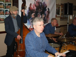'Engine' of Mahogany Hall Stompers at Farnborough Jazz Club (Kent) on 20th May 2015. (LtoR) Roger Curphey (double bass), Tim Huskisson (piano), Chris Marchant (drums) and just out of view) 'Southend Bob' Albutt (banjo). Photo by Mike Witt.