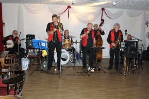 Phoenix Dixieland Jazz Band play for Farnborough Jazz Club on 19th August 2016. (LtoR) John Stuart (banjo), Bill Todd singing (trombone), Alan Clarke (drums), Mike Barry (trumpet), Roger Curphey (double bass), Charles Sherwood (tenor sax) and Dave Barnes (piano). Photo by Mike Witt. (wedding next day-hence decorations)