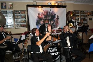 The Fenny Stompers at Farnborough Jazz Club's 'Battle of Brittain' Anniversary fancy dress party on 16th September 2016. The band perform in their pilot gear, to ''Me & Jane in a Plane'. (LtoR) Dave Arnold (Sousaphone), Dennis Vick (clarinet), Ken Joiner (drums), Dave Marchant (trumpet) and Brian Vick (banjo). With John Lee on trombone, goes flying about shooting around the audience. Photo by Mike Witt.